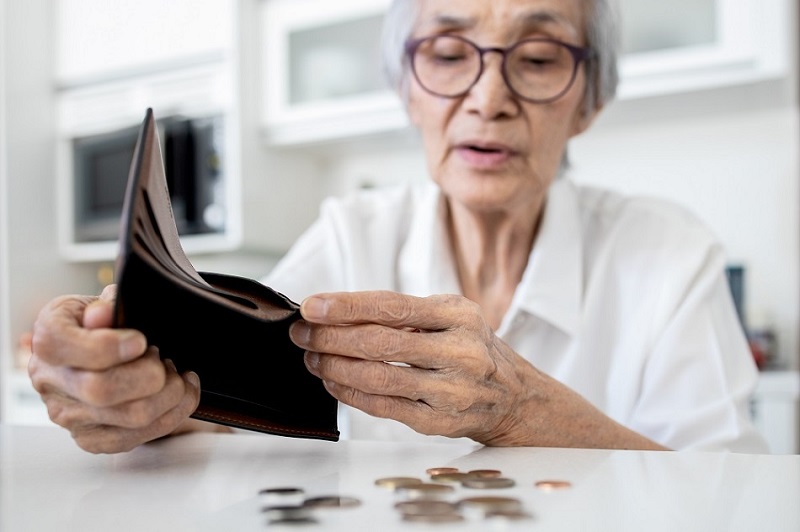 Senhora idosa mexe na carteira vazia em cima de uma mesa, onde estão algumas poucas moedas. A imagem ilustra como o dinheiro afeta a expectativa de vida do brasileiro.