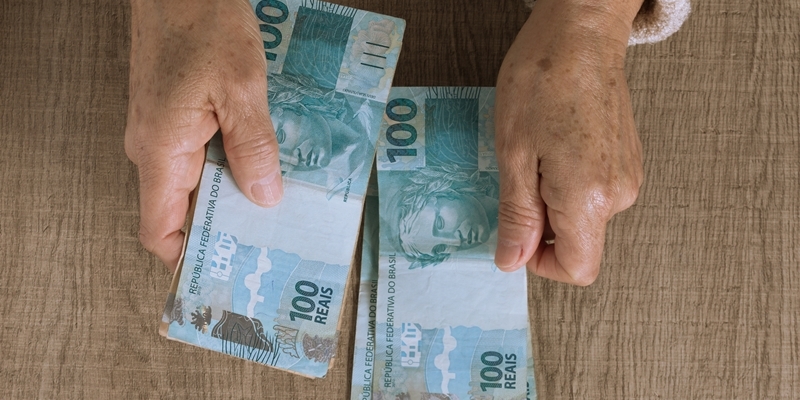 Uma senhora segurando notas de 100 reais. Imagem para ilustrar a matéria sobre 14º salário