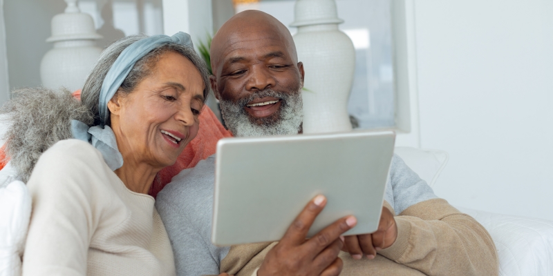 Um casal de idosos olhando um tablet e rindo. Imagem para ilustrar a matéria sobre se manter ativo após se aposentar.