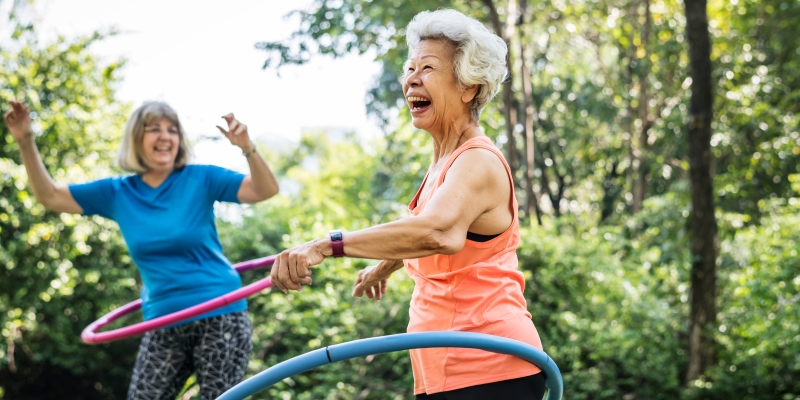 Duas idosas em um parque, brincando de bambolê. Imagem para ilustrar a matéria sobre se manter ativo após se aposentar.