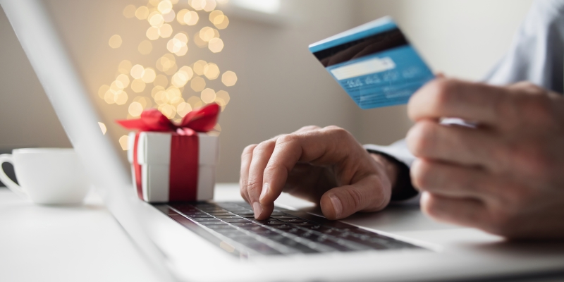 Uma pessoa no computador, segurando um cartão de crédito, simulando uma compra de Natal. Imagem para ilustrar a matéria sobre organização financeira.