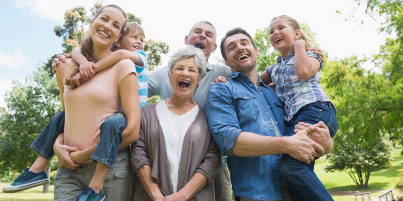 Uma família composta por avós, filhos e netos, em um parque, sorrindo. Imagem para ilustrar a matéria sobre poupar para os filhos.