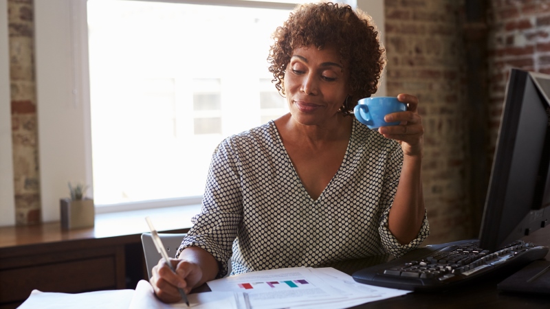 Uma mulher negra, sentada em uma mesa e fazendo anotações sobe o seu negócio de empreendedorismo maduro.