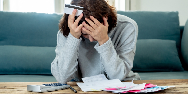 Uma mulher triste, sobre contas a pagar e uma calculadora. Na mão, um cartão de crédito. Imagem para ilustrar a matéria sobre o recorde de endividamento.