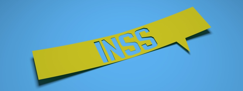 Uma placa de papel amarela sobre um fundo azul escrito INSS. Imagem para ilustrar a matéria sobre 5 curiosidades sobre os benefícios do INSS.