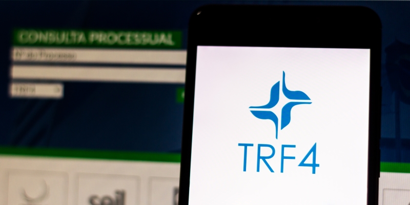 Um celular em destaque com a tela inicial do TRF4 e, ao fundo, a página do Tribunal Reginal Federal. Imagem para ilustrar a matéria sobre benefícios atrasados do INSS.
