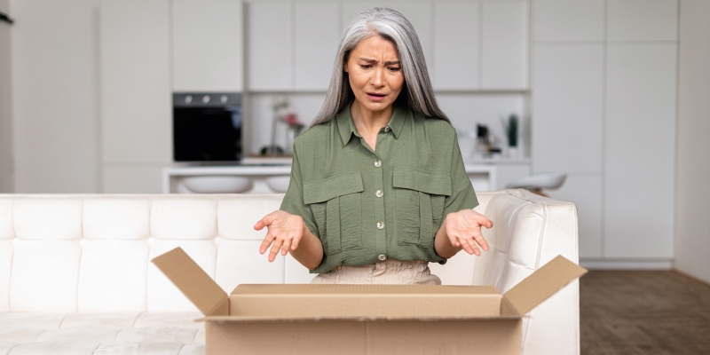 Uma mulher grisalha olhando para dentro da caixa de papelão e se sente infeliz e irritada com o pedido errado. Imagem para ilustrar a matéria sobre direito de arrependimento.
