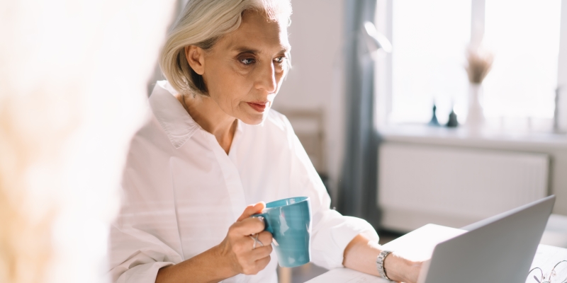 Uma mulher, com cerca de 60 anos, trabalhando em sua casa e tomando café. Imagem para ilustrar a matéria sobre estímulos criativos.