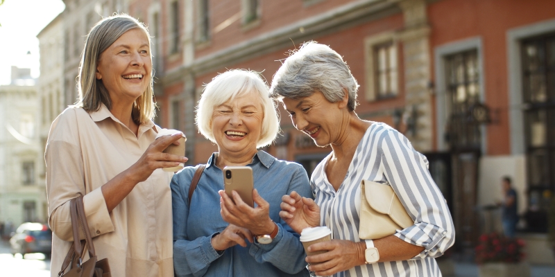 Um grupo de três mulheres viajando e sorrindo na rua. Imagem para ilustrar a matéria sobre intercâmbio depois dos 50 anos.