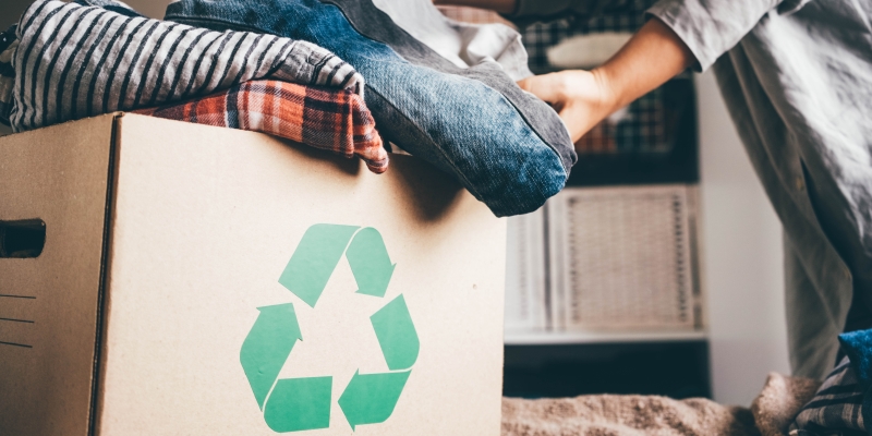 Uma mulher colocando roupas para doação em uma caixa de reciclagem. Imagem para ilustrar a matéria sobre a Semana do Meio Ambiente.