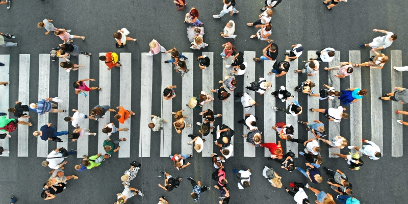 Dezenas de pessoas atravessando uma faixa de pedreste na rua, visto de cima. Imagem para ilustrar a matéria sobre expectativa de vida e aumento da população mundial.