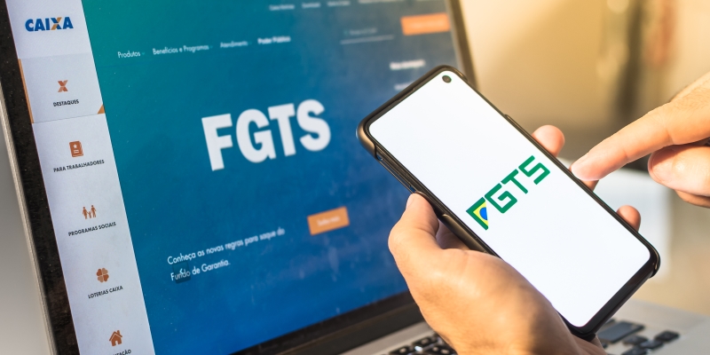 Um pessoas abrindo o aplicativo do FGTS e vendo o site do FGTS no computador. Imagem para ilustrar a matéria sobre o lucro do FGTS 2021.