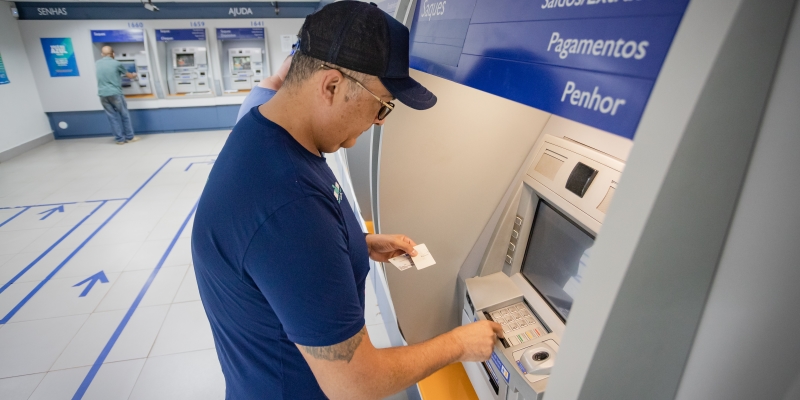 Um homem, em frente a um caixa eletrônico de banco, fazendo uma transição. Imagem para ilustrar a matéria sobre pagamento de atrasados do INSS.