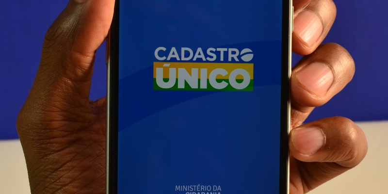 Um mão masculina segurando um celular. No aparelho, está aberto o aplicativo do Cadastro Único. Imagem para ilustrar a matéria sobre auxílio brasil de outubro.