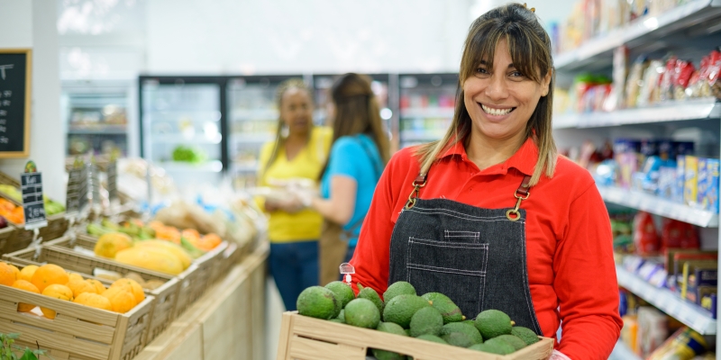 Uma mulher empreendedora vendendo abacates dentro de sua loja. Imagem para ilustrar a matéria sobre Caixa Pra Elas Empreendedoras.