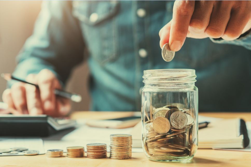 Uma pessoa colocando moedas em um pote de vidro. Imagem para retratar a matéria sobe Longevidade Financeira é o segredo para ter uma aposentadoria tranquila.